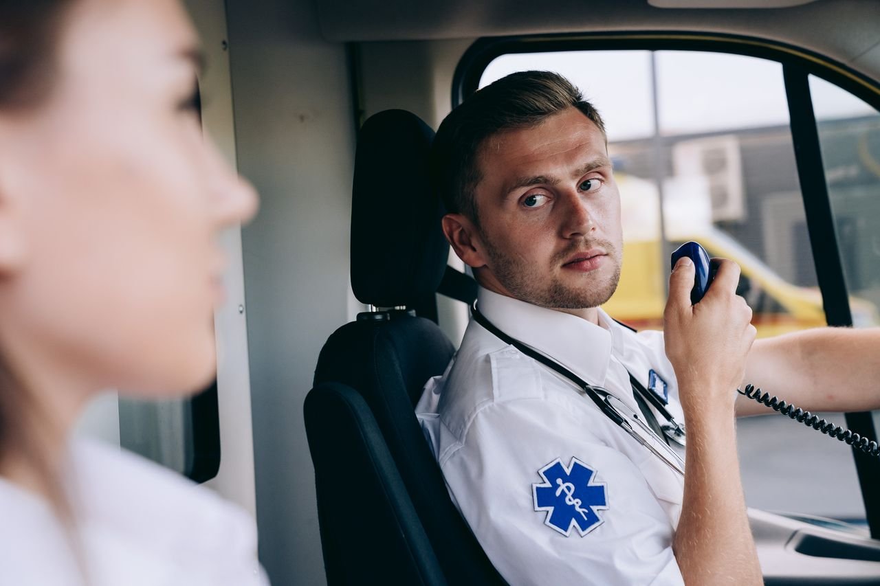 Paramedic using radio in ambulance, focused on communication and readiness.
